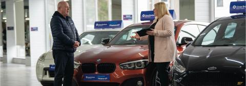 Dealer talking to a customer in a car showroom. 